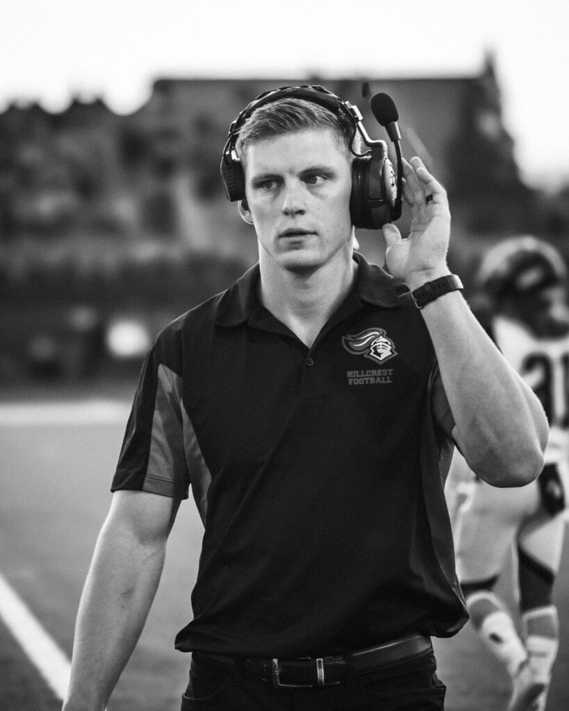 Black and white image of a football coach using a headset during a game.